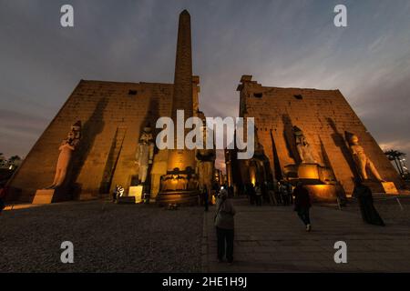Der Tempeleingang in Luxor, Ägypten mit einem Obelisk zu Ramses II und Statuen, die den Eingangsbereich flankieren. Nach Einbruch der Dunkelheit wird es dramatisch beleuchtet. Stockfoto
