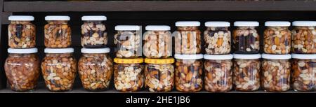 Verschiedene Nüsse in Honig. Ein Stand mit Produkten auf dem Straßenmarkt. Cashewkerne, Walnüsse, Mandeln, Haselnüsse und andere Nüsse in Honig oder Sirup in Gläsern. Stockfoto