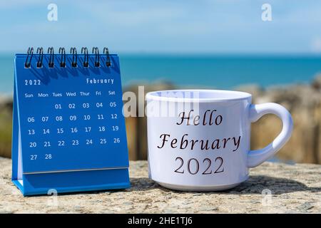 Hallo Februar 2022 auf einer weißen Kaffeetasse mit blauem Kalender geschrieben Stockfoto