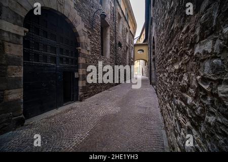 Dunkle, kleine mittelalterliche Gasse mit Kopfsteinpflaster und Steinmauern mitten in der Stadt. Stockfoto