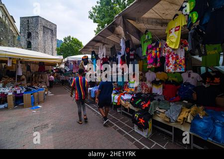 Viele verschiedene Waren wie Hemden und Schuhe werden auf dem Wochenmarkt neben der Porta Torre verkauft. Stockfoto