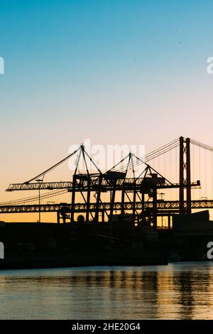 Silhouette von Kränen im Hafen von Lissabon, Portugal mit der Brücke vom 25. April im Hintergrund bei Sonnenuntergang Stockfoto