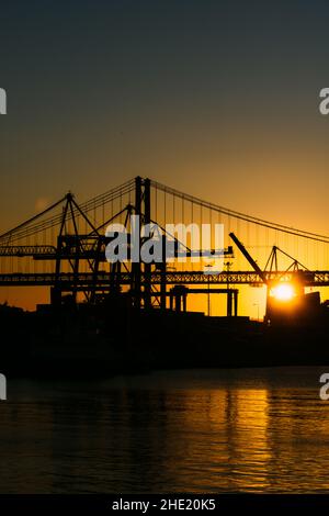 Silhouette von Kränen im Hafen von Lissabon, Portugal mit der Brücke vom 25. April im Hintergrund bei Sonnenuntergang Stockfoto