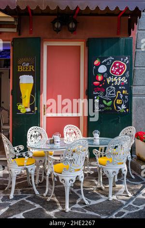 Schön angeordnetes Restaurant mit Tisch und Stühlen, handbemalte Werbetafeln für Bier und Pizza neben der Tür. Stockfoto