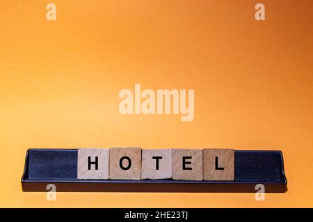 HOTEL. Wort auf quadratischen Holzfliesen mit orangefarbenem Hintergrund geschrieben. Horizontale Fotografie. Stockfoto