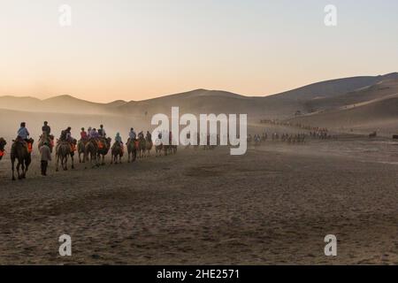 DUNHUANG, CHINA - 21. AUGUST 2018: Touristen reiten auf Kamelen in der Singing Sands Dune in der Nähe von Dunhuang, Provinz Gansu, China Stockfoto