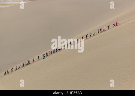 DUNHUANG, CHINA - 21. AUGUST 2018: Touristen klettern auf die Singende Sanddüne in der Nähe von Dunhuang, Provinz Gansu, China Stockfoto