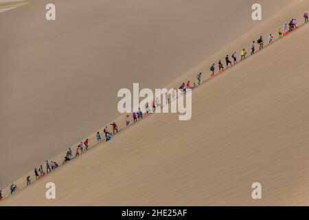 DUNHUANG, CHINA - 21. AUGUST 2018: Touristen klettern auf die Singende Sanddüne in der Nähe von Dunhuang, Provinz Gansu, China Stockfoto