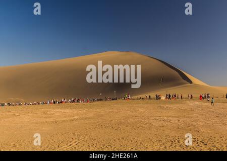 DUNHUANG, CHINA - 21. AUGUST 2018: Touristen in der Singing Sands Düne in der Nähe von Dunhuang, Provinz Gansu, China Stockfoto