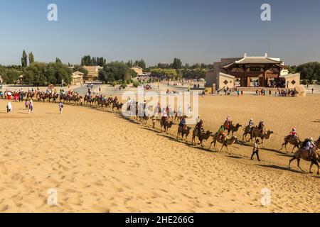 DUNHUANG, CHINA - 21. AUGUST 2018: Touristen reiten auf Kamelen in der Singing Sands Dune in der Nähe von Dunhuang, Provinz Gansu, China Stockfoto
