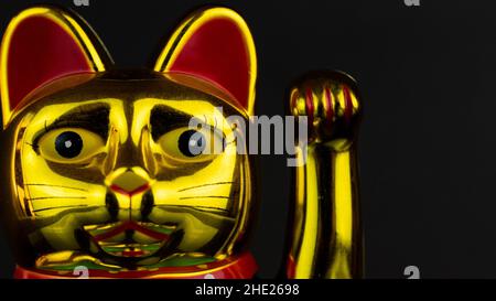 Nahaufnahme einer goldenen Maneki-Neko-Katze auf einem balckigen Hintergrund Stockfoto