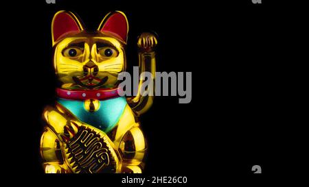 Nahaufnahme einer goldenen Maneki-Neko-Katze auf einem balckigen Hintergrund Stockfoto