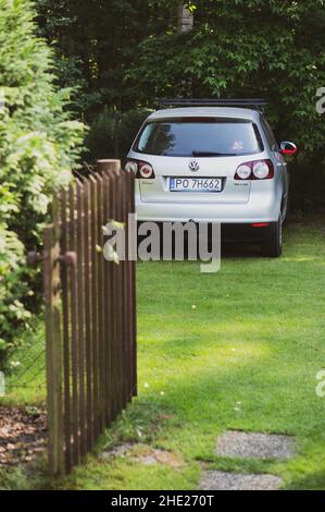 Vertikaler Schuss Volkswagen Golf Plus graues Auto auf grünem Gras hinter einem Holzzaun geparkt Stockfoto