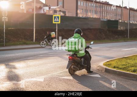 Krasnodar, Russland - Januar 06 2022: Food Delivery Boy auf Roller mit isothermen Lebensmittel-Fall Stockfoto