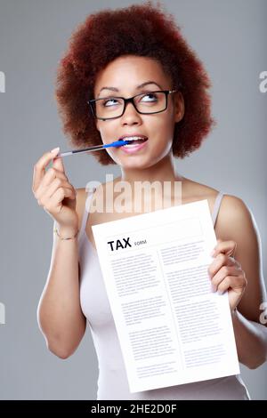 Nachdenkliche junge schwarze Frau, die eine Brille trägt und mit einem Stift an ihrem Mund steht und einen Steuerbeleg hält Stockfoto