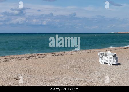 Blick auf den Strand von Uchkuevka mit weißen Liegestühlen, Foto der Sommerlandschaft an der Schwarzmeerküste an einem sonnigen Sommertag, Krim Stockfoto