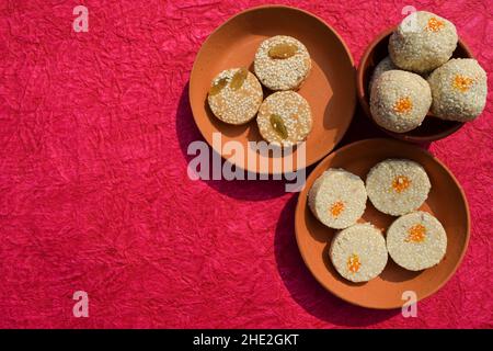 Tilgul ladoo mit Til gur baati und Til mawa bati auf hellem rosafarbenem Hintergrund Leerraum, um sankranti Wünsche und Grüße mit Schriftarten und Text zu schreiben. S Stockfoto