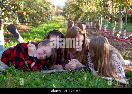 Drei Sommersprossen-Kinder und ihre rothaarige Mutter lagen auf dem Boden in einem Obstgarten und hatten Spaß Stockfoto