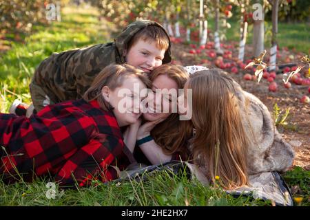 Eine rothaarige Mutter lächelt und erhält Küsse von ihren drei Sommersprossen Stockfoto