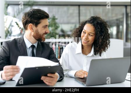 Zwei erfolgreiche multiethnische Kollegen arbeiten an einem Projekt zusammen. Kaukasischer erfolgreicher Mann, ceo-Unternehmen diskutiert Geschäftsstrategie mit afroamerikanischen Kollegin in einem modernen Büro Stockfoto