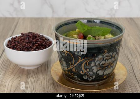 Würzige Schüssel mit grünem, geröhtem und Hühnchen, serviert mit einer Seite roten Reises. Stockfoto