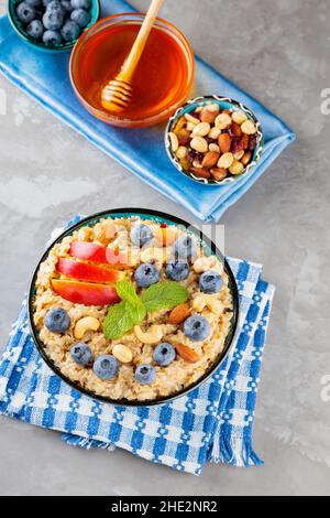 Haferflocken und die Zutaten für ein gesundes Frühstück auf grauem Hintergrund. Gekochte Haferflocken, Heidelbeeren, Nüsse, Apfelscheiben und Honig. Gesundes Frühstück Stockfoto