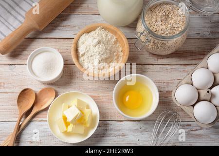 Rahmen aus Zutaten zum Backen auf weißem Hintergrund. Mehl, Eier, Zucker und Milch in weißen und hölzernen Schüsseln. Koch- und Backkonzept. Stockfoto