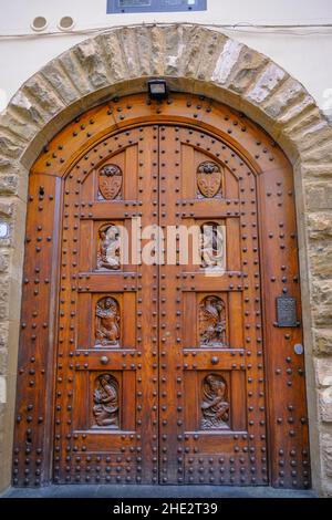 Wunderschöne Holztür in Florenz mit Figuren, die aus der Nähe über die Ziegelmauer geschnitten wurden. Gebäude außen, Fassade, Eingang Stockfoto