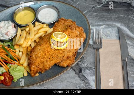 Hühnchen-Schnitzel und gebratene Kartoffeln auf dem Teller auf Marmorboden. Draufsicht, flach liegend Stockfoto