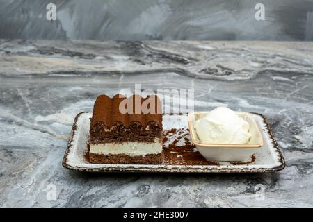 Eine Scheibe Tiramisu und Eis in einem Serviergeschirr aus Porzellan auf einem Marmorboden Stockfoto