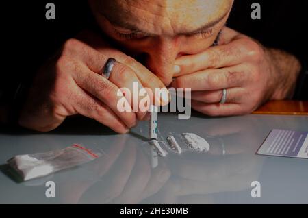 Dieser Mann schnaucht Kokainpulver mit gerollter Banknote. Betäubungsmittel-Konzept. Stockfoto