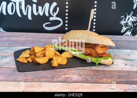 Dorfbrot-Sandwich mit Hähnchenstreifen paniert mit Mayonnaise, Tomaten und Salat mit gebratenen Kartoffelkeilen Stockfoto