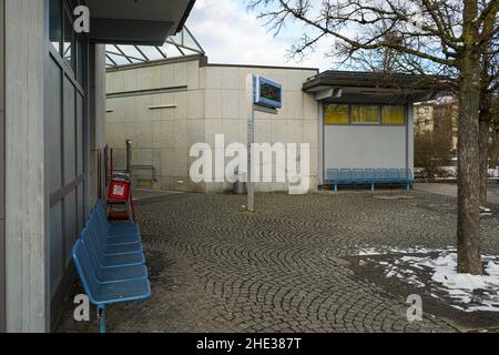 Leere Bänke an einer Bushaltestelle während der Corona-Pandemie in Deutschland. Zwischen einem elektronischen Zeitplananzeiger auf einem Stapel. Wir haben einen roten Zeitungsstand verlassen. Stockfoto