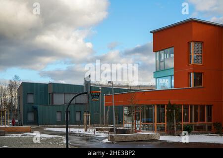 Ein rotes und ein grünes Schulgebäude an der Waldorfschule Campus Rudolf Steiner in München. Vorne ein Basketballplatz mit einem Reifen. Einige Fenster schließen sich. Stockfoto