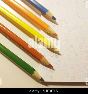 Buntstifte auf weißem Papier mit gezeichneten Herzen. Stockfoto