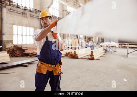 Serious Mann Baumeister trägt Holzbrett auf der Baustelle Stockfoto