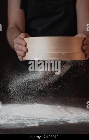 Männerhände sieben Mehl durch ein Sieb auf schwarzem Grund Stockfoto