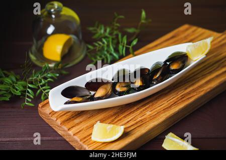 Weißer Teller mit Muschel im Waschbecken und Zitronenscheibe auf Holztisch von oben Stockfoto