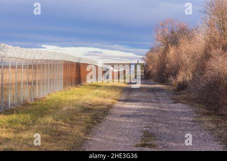Zaun mit Stacheldraht entlang einer Staatsgrenze mit dunklen Wolken Stockfoto