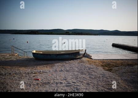 Ein kleines Ruderboot ruht bei Sonnenaufgang an einer sandigen Küste des Ozeans. Stockfoto