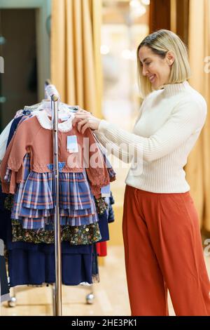 Frau mittleren Alters, die Kleidung für ihre Kinder in einem Kinderbekleidungsgeschäft kauft. Stockfoto