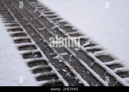 Spur eines Autoreifens auf dem Schnee, der den Asphalt auf der Straße bedeckt, am Wintertag aus nächster Nähe Stockfoto