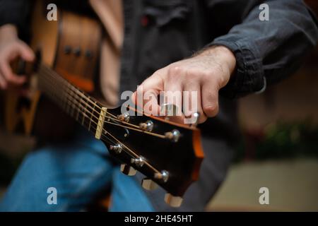 Ein Typ spannt mit Nahaufnahme einen Akkord auf eine akustische Gitarre Stockfoto