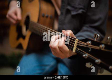 Ein Typ spannt mit Nahaufnahme einen Akkord auf eine akustische Gitarre Stockfoto