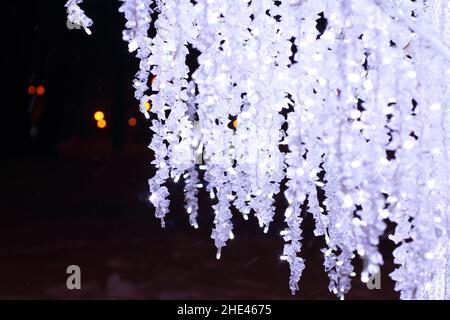 Leuchtende LED-Lampen Girlanden in einem verschneiten Park in der Nacht. Girlanden in Form von Bäumen. Stockfoto