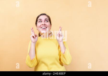 Warten auf einen besonderen Moment, Daumen drücken, Wunsch machen. Junge Frau auf hellorangefarbenem Hintergrund. Stockfoto