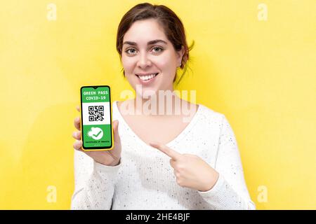 Lächelnde, positive junge Frau zeigt einen digitalen grünen Pass auf dem Smartphone. Stockfoto