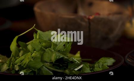 Frische Petersilie auf dem Tisch in der Nähe der alten Holzschüssel. Nahaufnahme der männlichen Hand nehmen Bund von grünen Blättern während des Kochvorgangs. Stockfoto