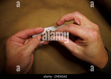 Ein Mann rollt ein Zigarettenpapier und füllt es mit losem Tabak Stockfoto