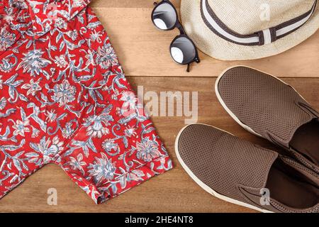 Ein Paar Sneaker ein Hemd mit Blumen, Sonnenbrille und einem Hut auf einem hölzernen Hintergrund Sommerkleidung Konzept. Stockfoto